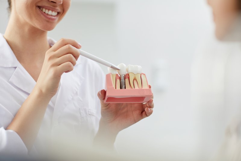 A dentist holding a dental implant model and pointing to it with a pen